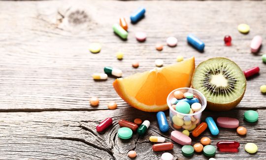 Ripe fruits and colorful pills on wooden table